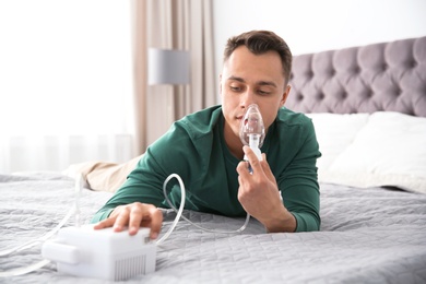 Young man with asthma machine on bed in light room