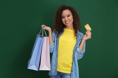 Young African-American woman with credit card and shopping bags on color background. Spending money