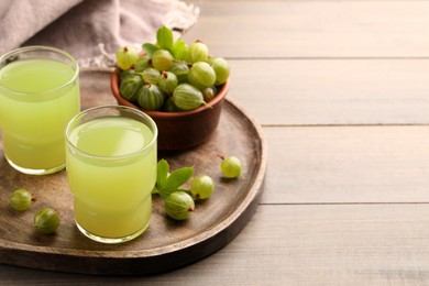 Photo of Tasty gooseberry juice and fresh berries on wooden table. Space for text