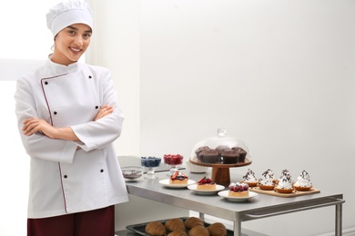 Female chef near table with different pastries in kitchen