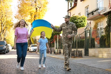 Photo of Soldier in military uniform with his family running and holding Ukrainian flag on city street