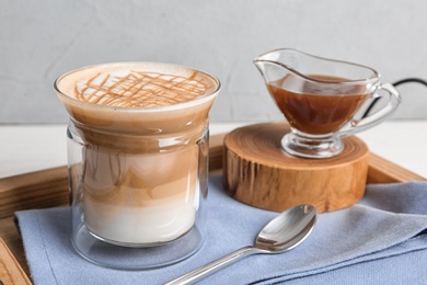 Glass of caramel macchiato and gravy boat with sauce on table