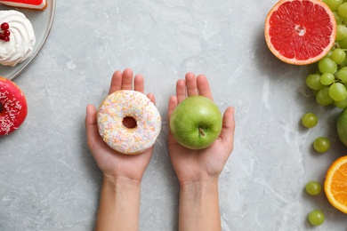 Photo of Concept of choice. Top view of woman holding apple and doughnut at grey table, closeup