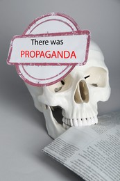 Photo of Information warfare concept, media propaganda influence. Human skull with stump and newspaper on grey background
