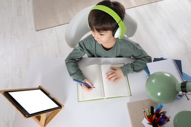Cute little boy with modern tablet studying online at home, above view. E-learning
