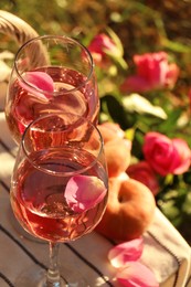 Photo of Glasses of delicious rose wine with petals on white picnic blanket outside