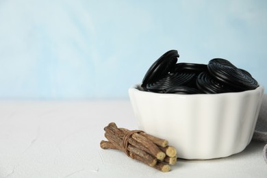 Tasty black candies and dried sticks of liquorice root on white table. Space for text