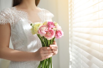 Bride with beautiful ranunculus bouquet indoors, closeup. Space for text