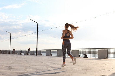 Young woman running on pier near river in morning. Space for text