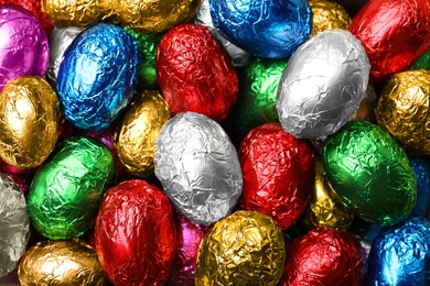 Chocolate eggs wrapped in colorful foil as background, top view
