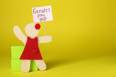Photo of Gender pay gap. Wooden figure of woman with sign on yellow background, space for text