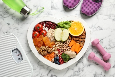 Heart shaped tray with healthy products and sports equipment on marble background, flat lay