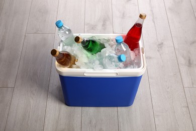 Blue plastic cool box with ice cubes and refreshing drinks on wooden floor