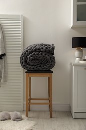 Wooden stool with rolled chunky knit blanket in room
