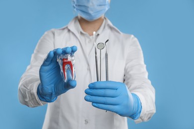 Dentist holding tooth model and tools on light blue background, closeup