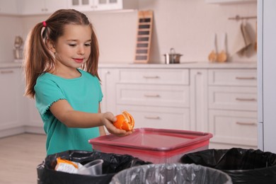 Little girl throwing tangerine peel into trash bin in kitchen. Separate waste collection