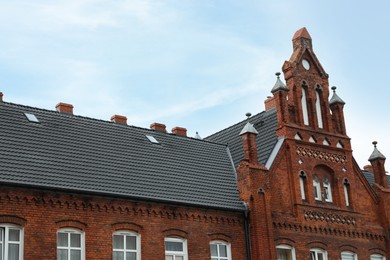 Beautiful red brick building with grey roof against blue sky, low angle view