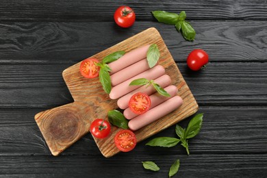 Fresh raw vegetarian sausages with basil and tomatoes on black wooden table, flat lay