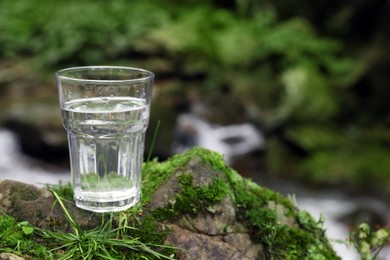 Glass of fresh water on stone with moss near stream. Space for text