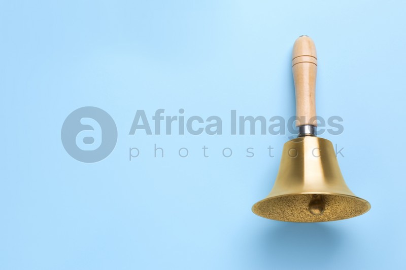 Golden school bell with wooden handle on light blue background, top view. Space for text