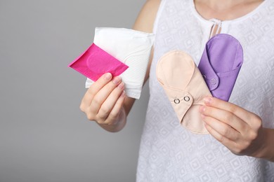 Woman holding disposable and reusable cloth menstrual pads on grey background, closeup