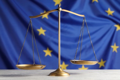 Scales of justice on light grey table against European Union flag
