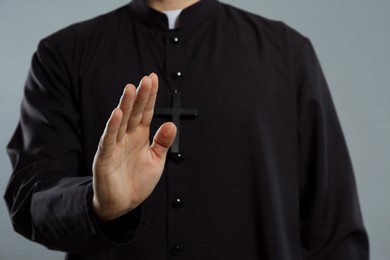 Priest making blessing gesture on grey background, closeup