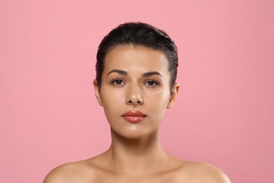Woman with cream around eye on pink background. Skin care