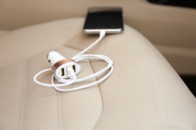 Photo of Adapter with connected charging cable and mobile phone in car, closeup
