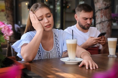 Young woman having boring date with guy in outdoor cafe