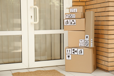 Cardboard boxes with different packaging symbols on porch near entrance, space for text. Parcel delivery
