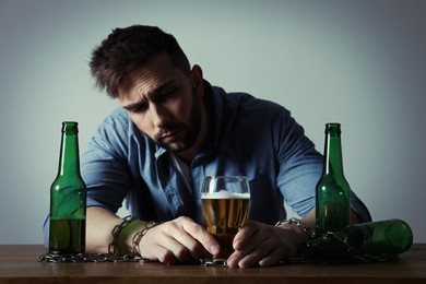 Addicted man chained to glass of alcoholic drink at wooden table
