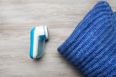 Photo of Modern fabric shaver for lint removing and sweater on wooden table, flat lay