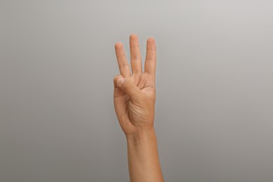 Teenage boy showing three fingers on light grey background, closeup