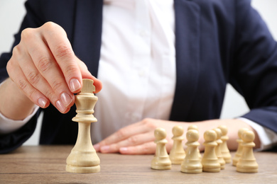 Woman with chess piece at wooden table, closeup. Career promotion concept