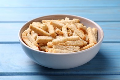 Crispy wheat rusks in bowl on light blue wooden table