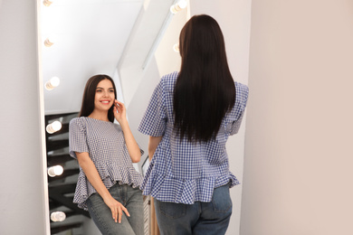 Young attractive woman looking at herself in stylish mirror at home