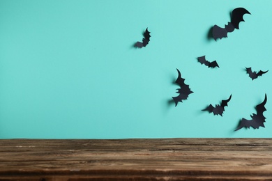 Empty wooden table near light blue wall decorated with paper bats, space for text. Halloween celebration