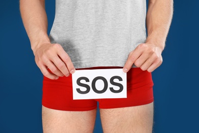 Man holding SOS sign on blue background, closeup. Urology problems