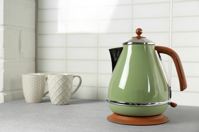 Stylish electric kettle and tea cups on grey table against white wall