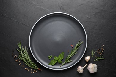 Dark plate with herbs, peppercorns and garlic on black table, flat lay