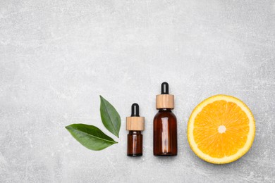 Bottles of essential oil with orange slice and leaves on grey table, flat lay