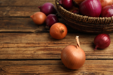 Onion bulbs and basket on wooden table. Space for text