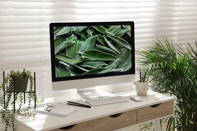 Comfortable workplace with modern computer and green plants in room. Interior design