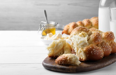 Photo of Homemade braided bread with sesame seeds on white wooden table, space for text. Traditional challah