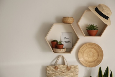 Hexagon wooden shelves with beautiful plants and accessories on light wall. Space for text