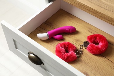 Fluffy handcuffs and vibrator in open wooden drawer. Sex toys