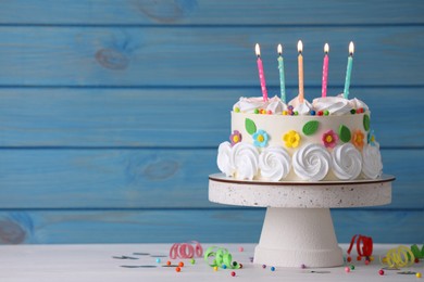 Delicious birthday cake and party decor on white wooden table against light blue background, space for text