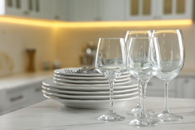 Photo of Clean glasses, dishware and cutlery on white marble table in kitchen