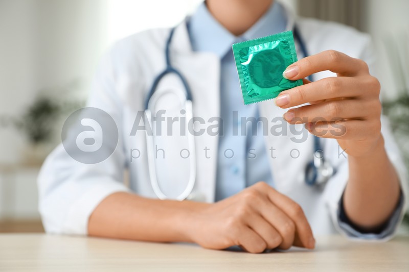 Female doctor holding condom at table indoors, closeup. Safe sex concept